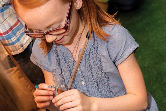 The Joyful Road Station Photo: A young girl smiles as she places her cross made of nails on a chin around her neck.