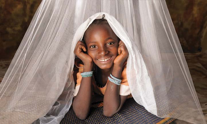 girl smiles at the camera from under a mosquito net