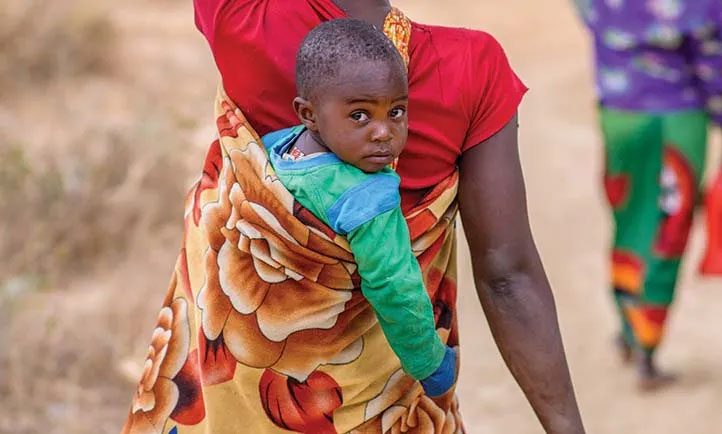 zambian baby rides in a pack on his or her mother's back and looks curiously back at camera