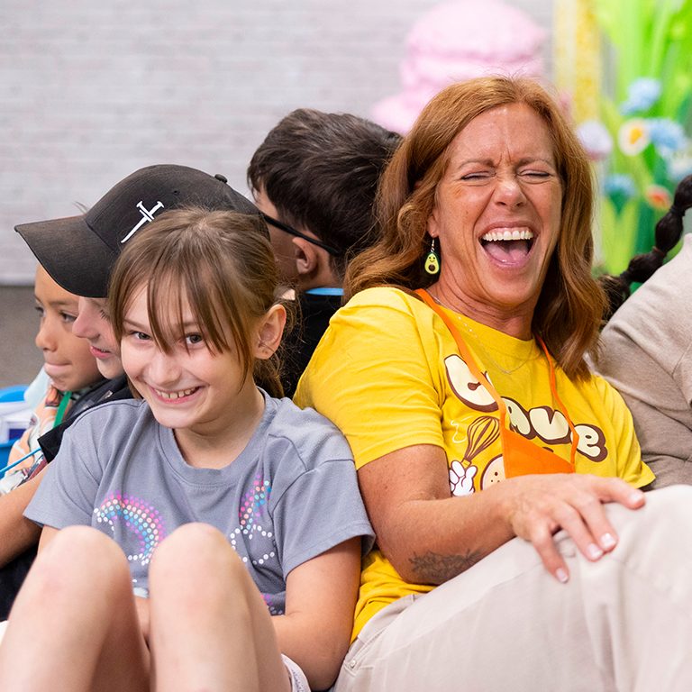 VBS leader and girl sitting back to back laughing